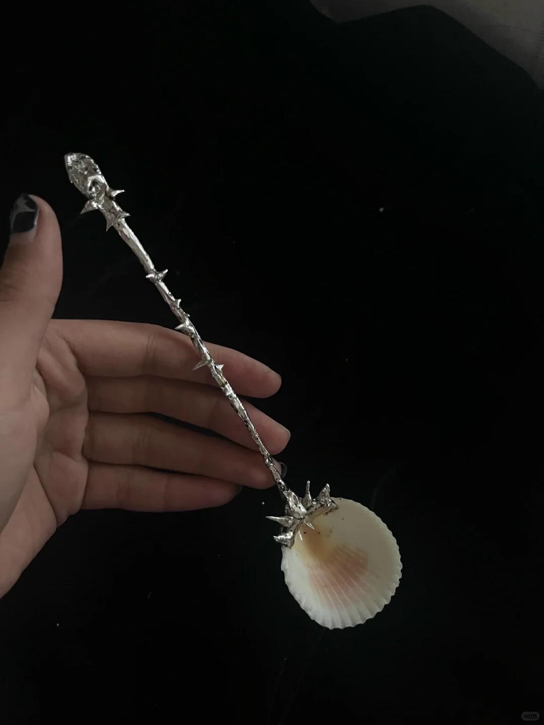 Close-up of a decorative shell spoon showing the ornate metal handle and shell bowl.