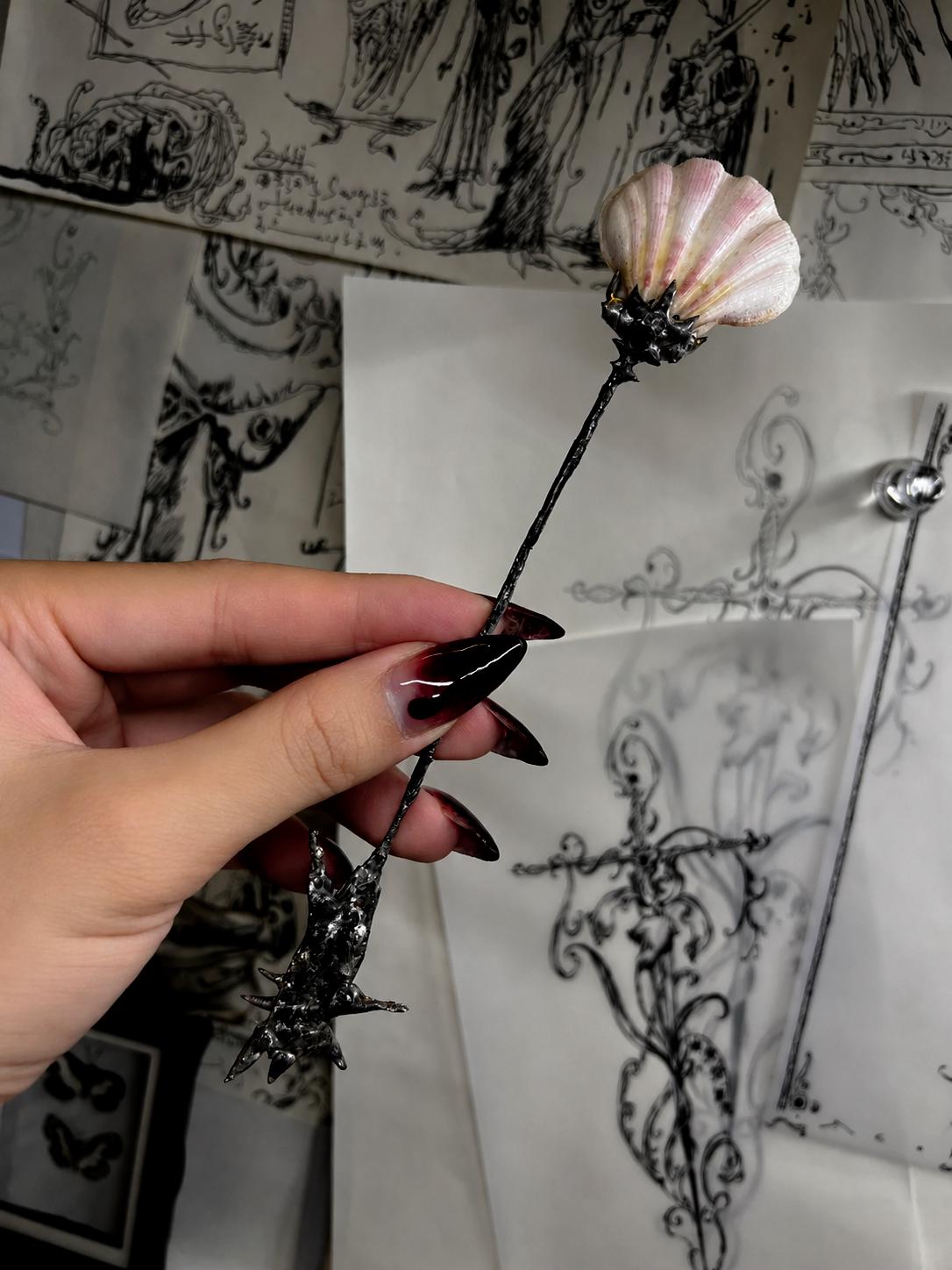 Decorative shell spoon with a pink shell bowl and ornate silver-tone handle, held in a hand.