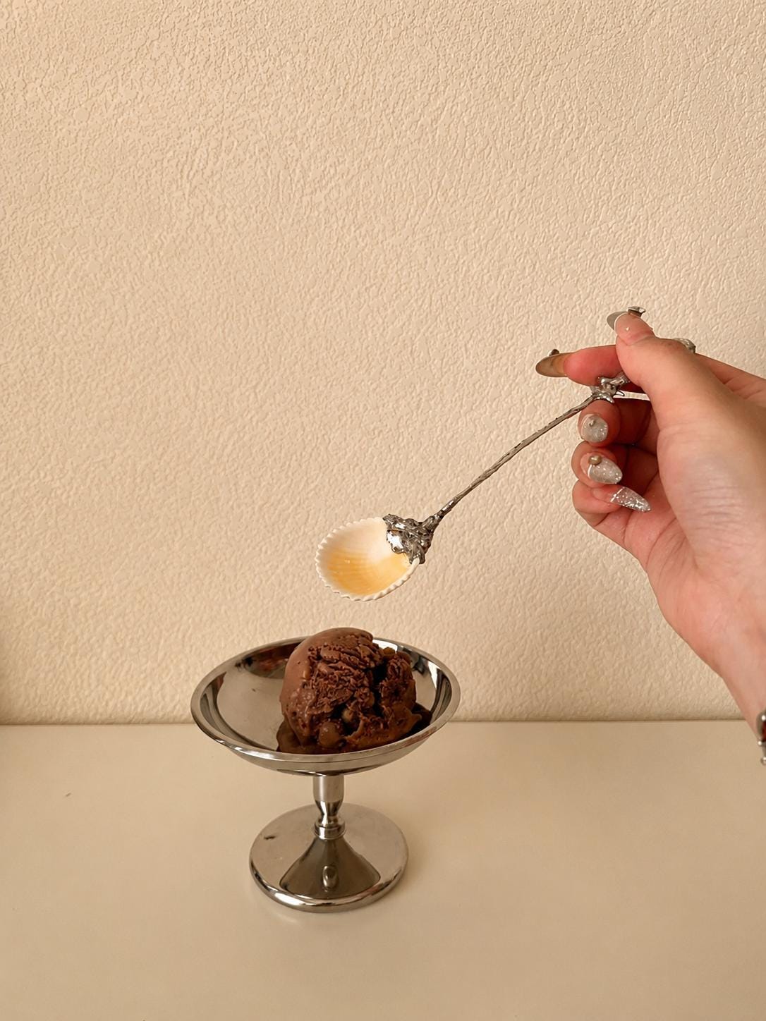 Decorative shell spoon shown above a small plated cake in a styling scene.