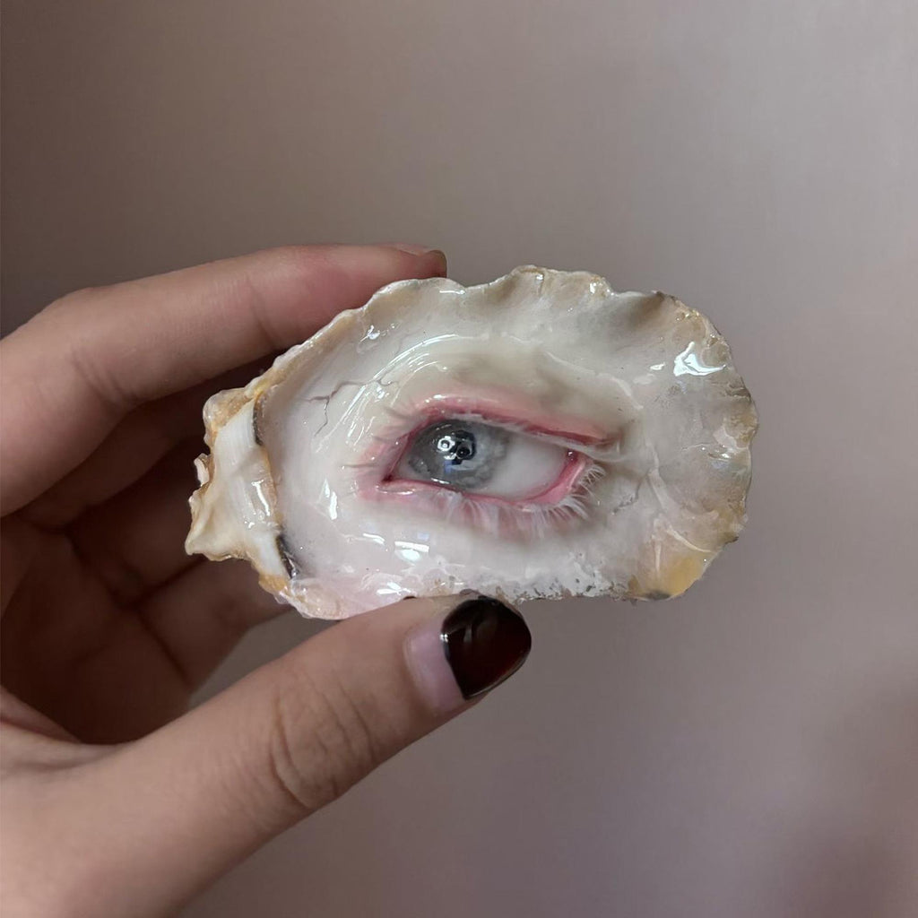 Pearl-Free White-Water Blue Oyster Eye held in a hand, showing the pale blue iris and pink eyelid.