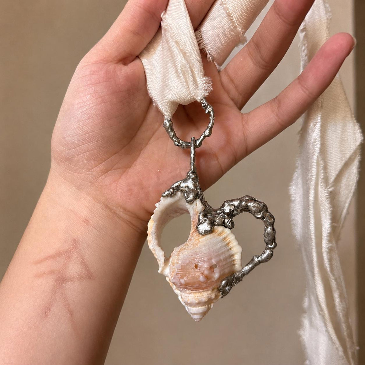 Spiked Conch Loop Talisman on ivory ribbon held across a hand.