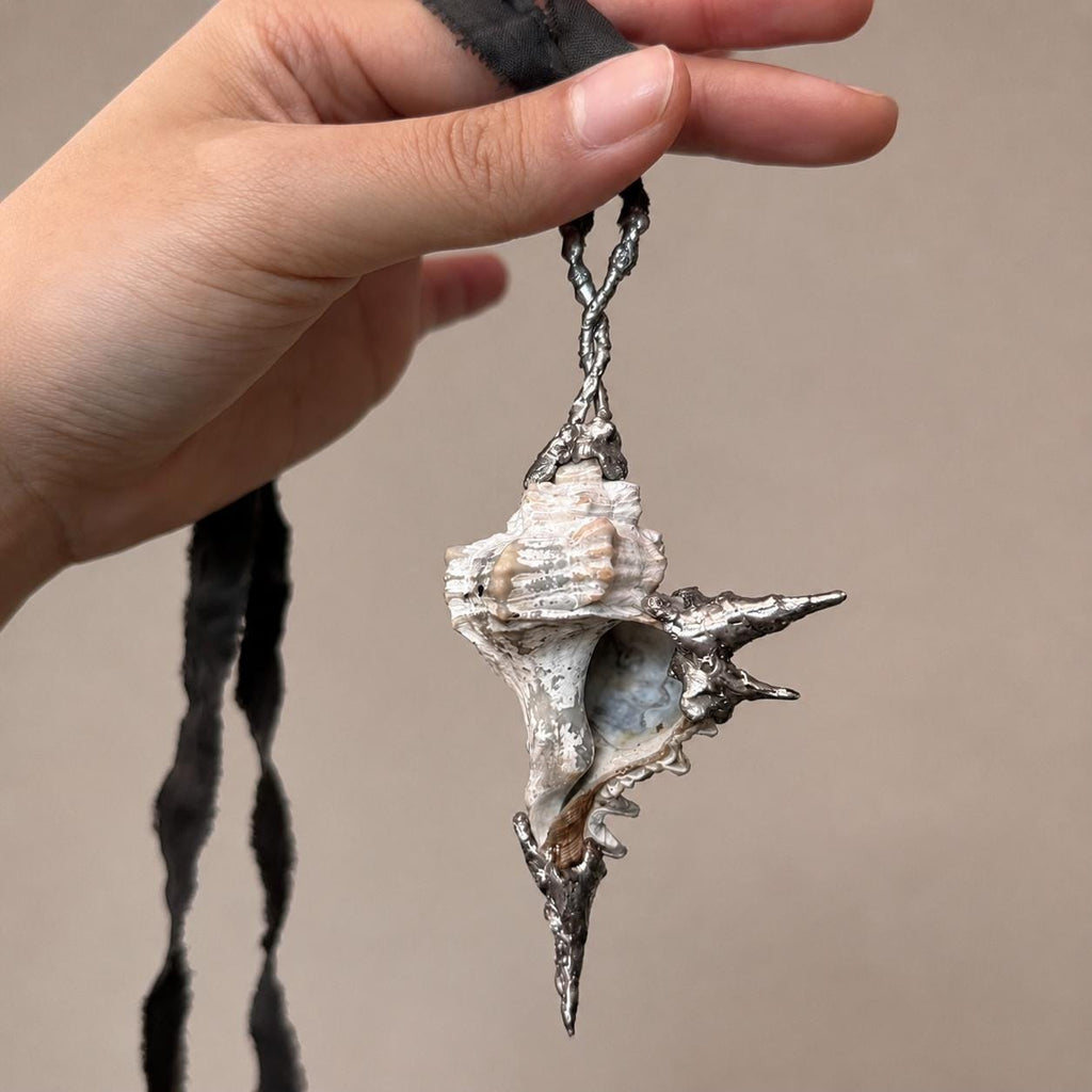 Reverse of the Spiked Conch Loop Talisman hanging from dark cord.