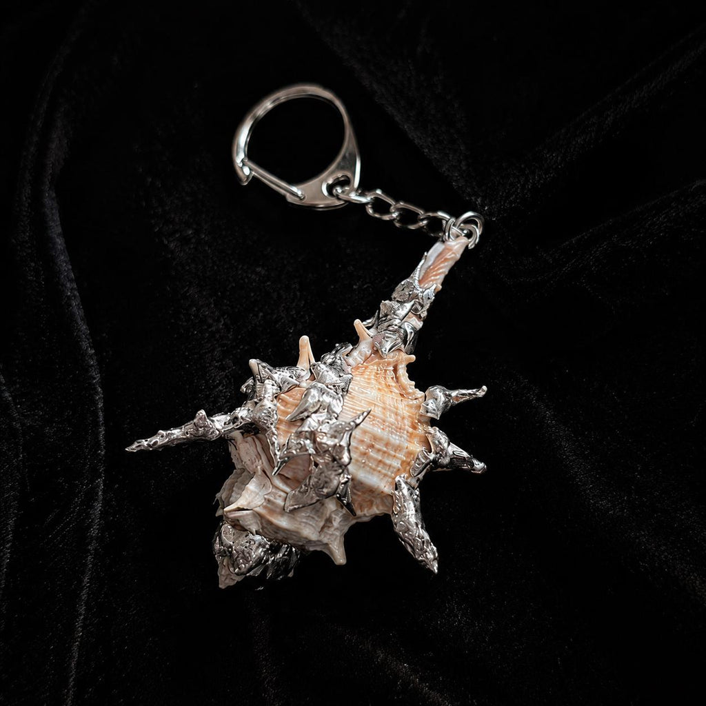 Spiked Conch Loop Talisman attached to a metal keychain on black velvet.