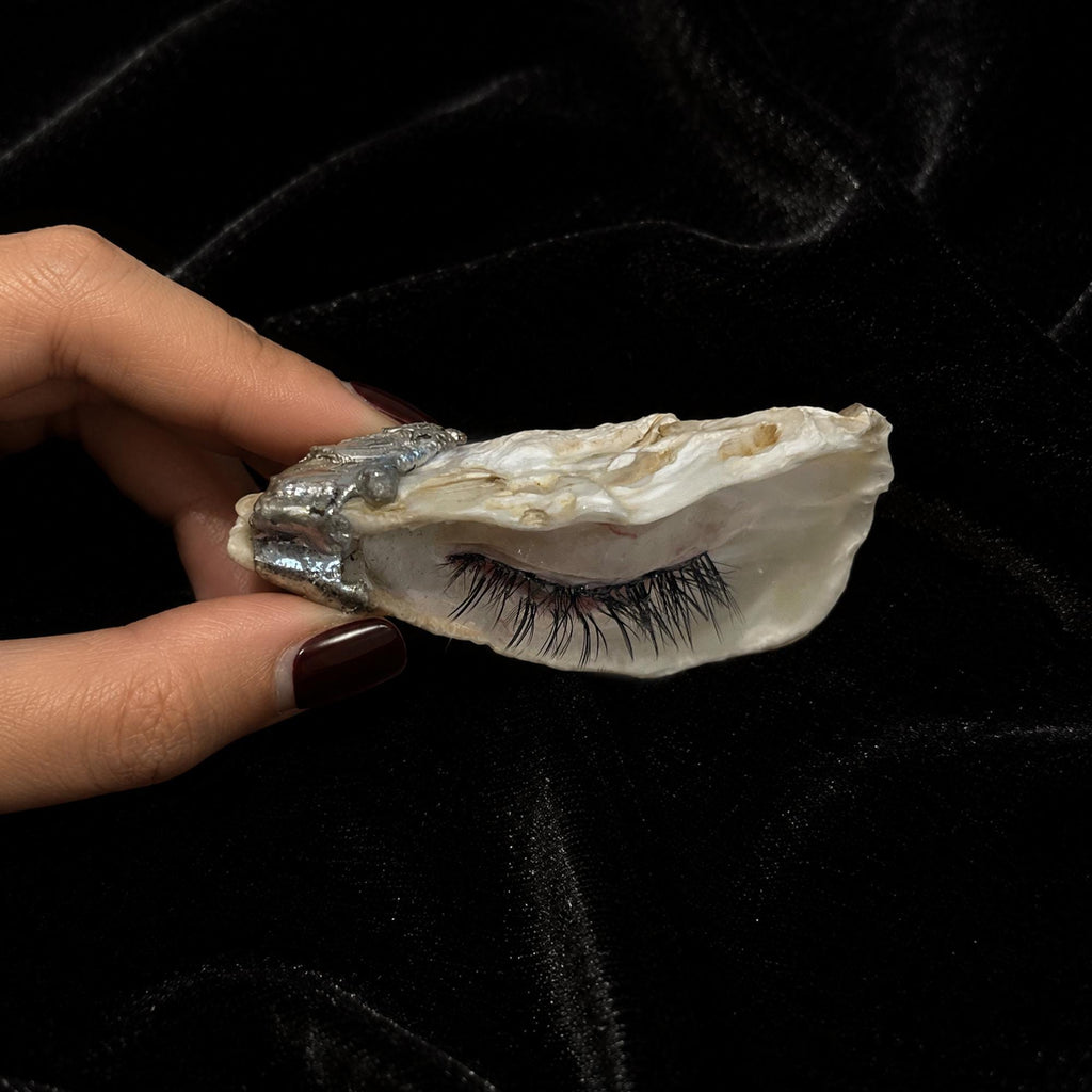 Side view of Nyra Black-Lash Oyster Eye held in a hand, showing shell thickness and long lashes.
