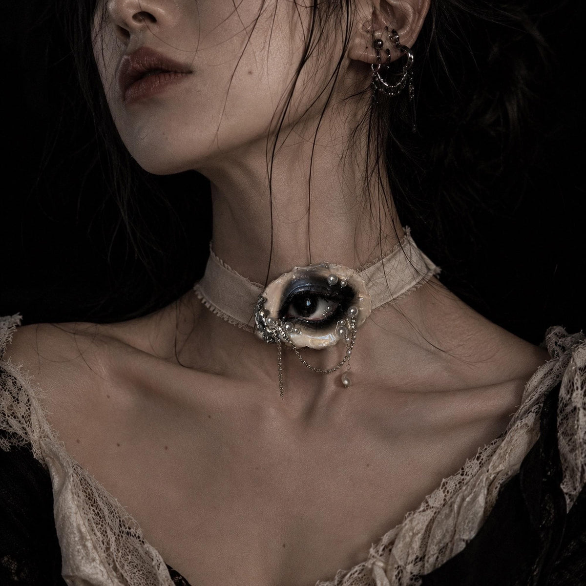 Lilith Veil Black Smoky oyster eye worn as an ivory-ribbon choker above a pale blouse.