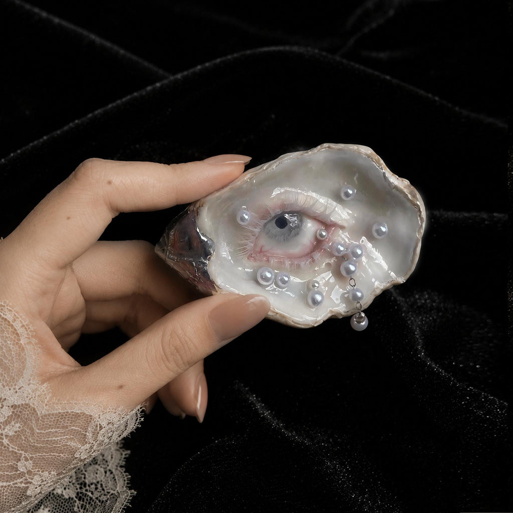 Nyra Unimpressed Gaze oyster eye held between fingers against a light wall.