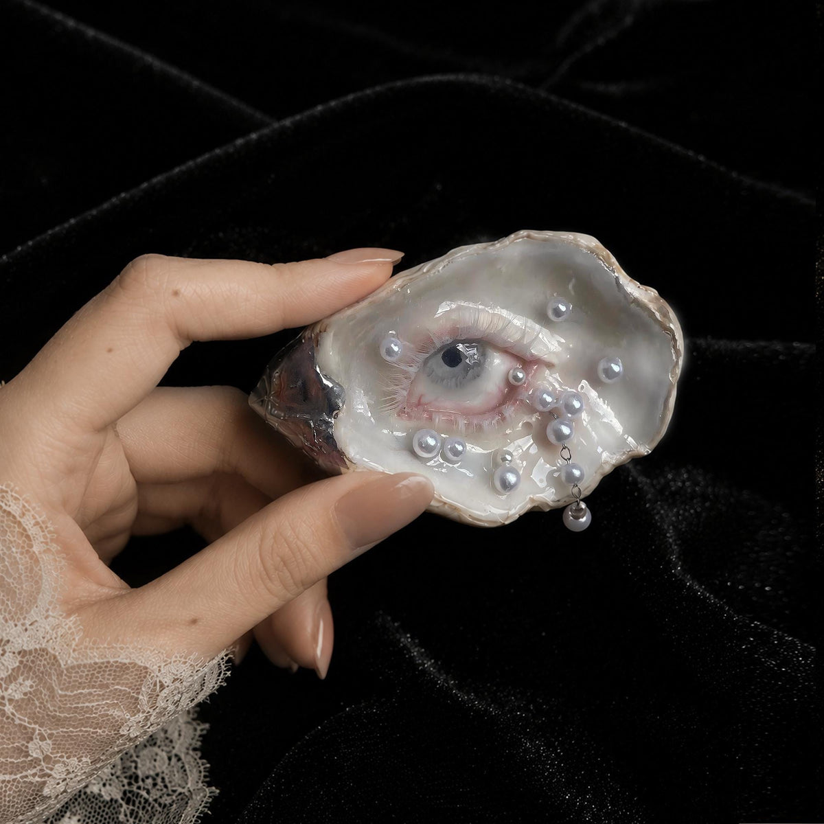 Nyra Unimpressed Gaze oyster eye held between fingers against a light wall.