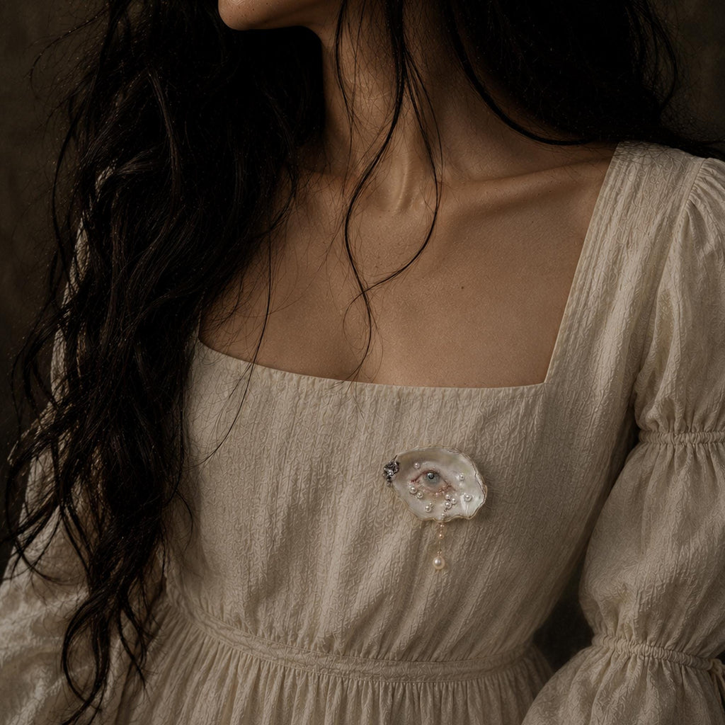 Nyra Unimpressed Gaze shell-eye brooch worn on a pale gathered blouse.