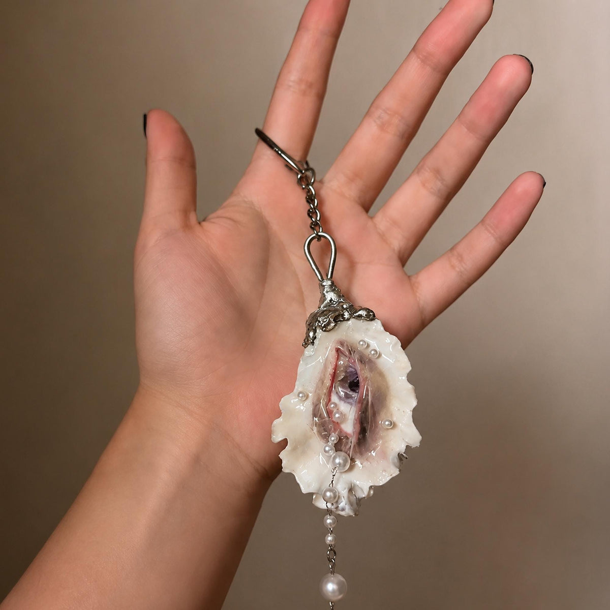 Nyra Ash Grey-Lash oyster eye keychain resting across a hand to show its scale.