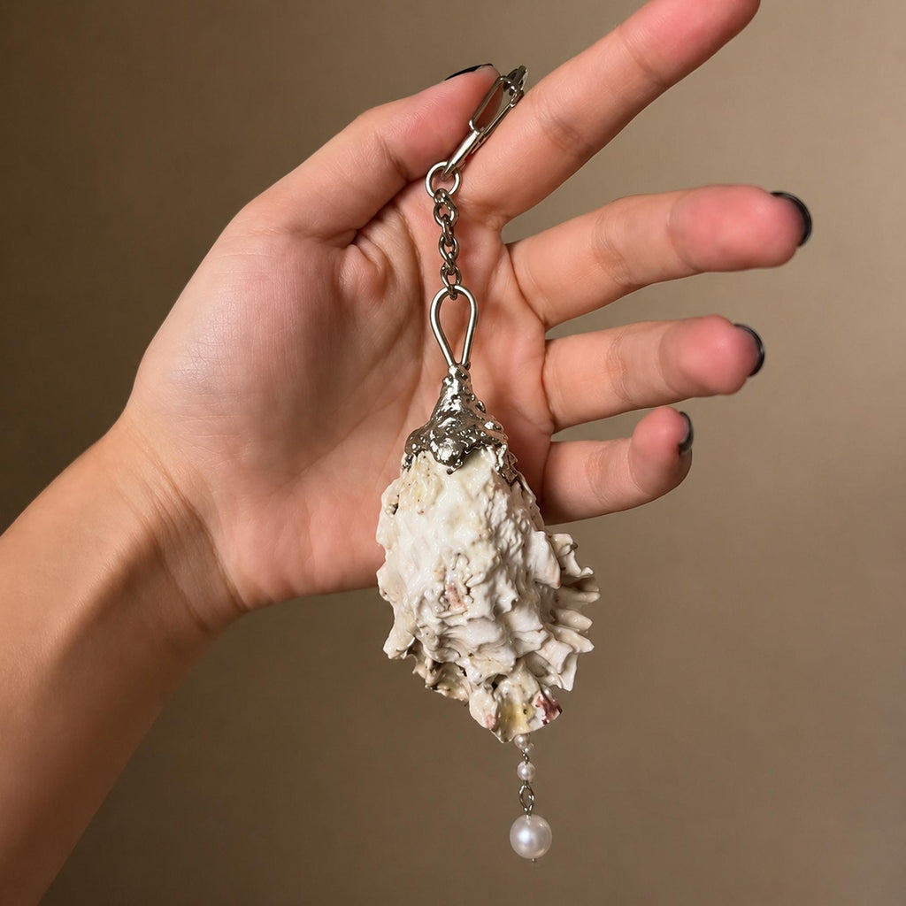 Reverse of the Nyra Ash Grey-Lash keychain showing the natural shell exterior.