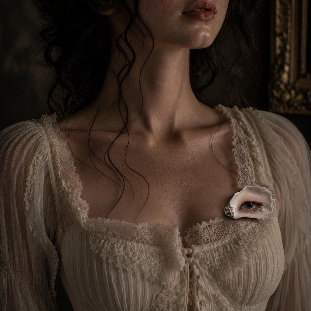 Nyra Tender Gaze shell-eye brooch worn on a pale gathered blouse.