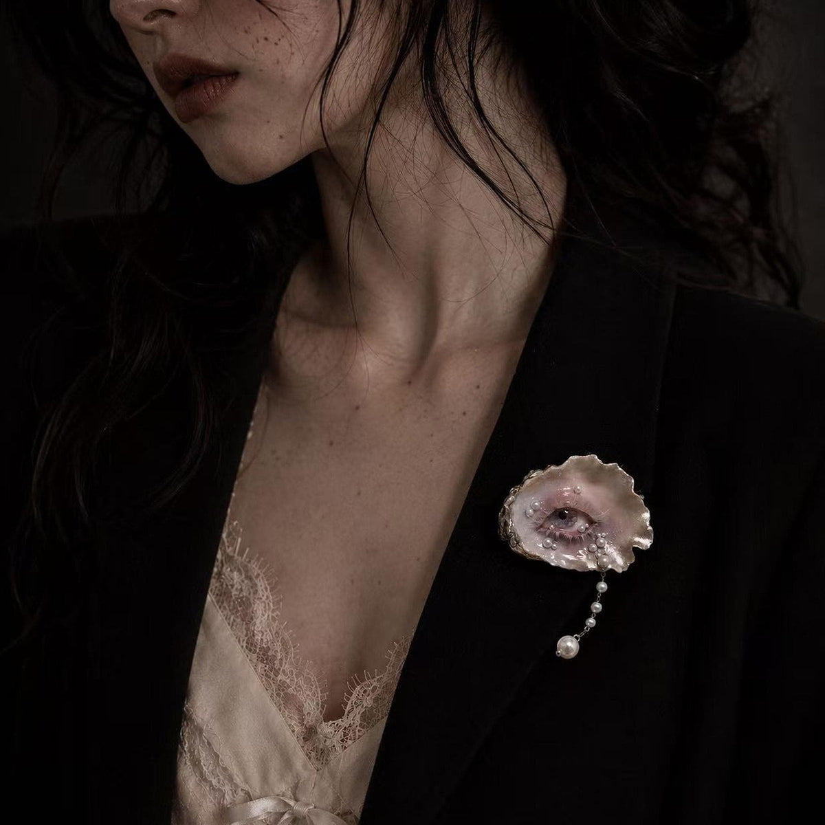 Nyra Lavender Gaze shell-eye brooch worn on a dark blazer over a pale blouse.