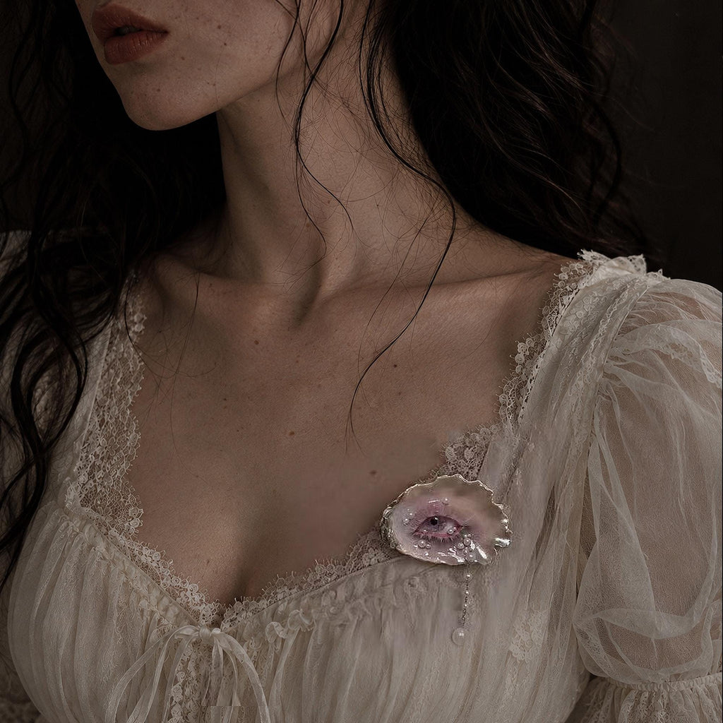 Nyra Lavender Gaze shell-eye brooch worn on a gathered ivory blouse.