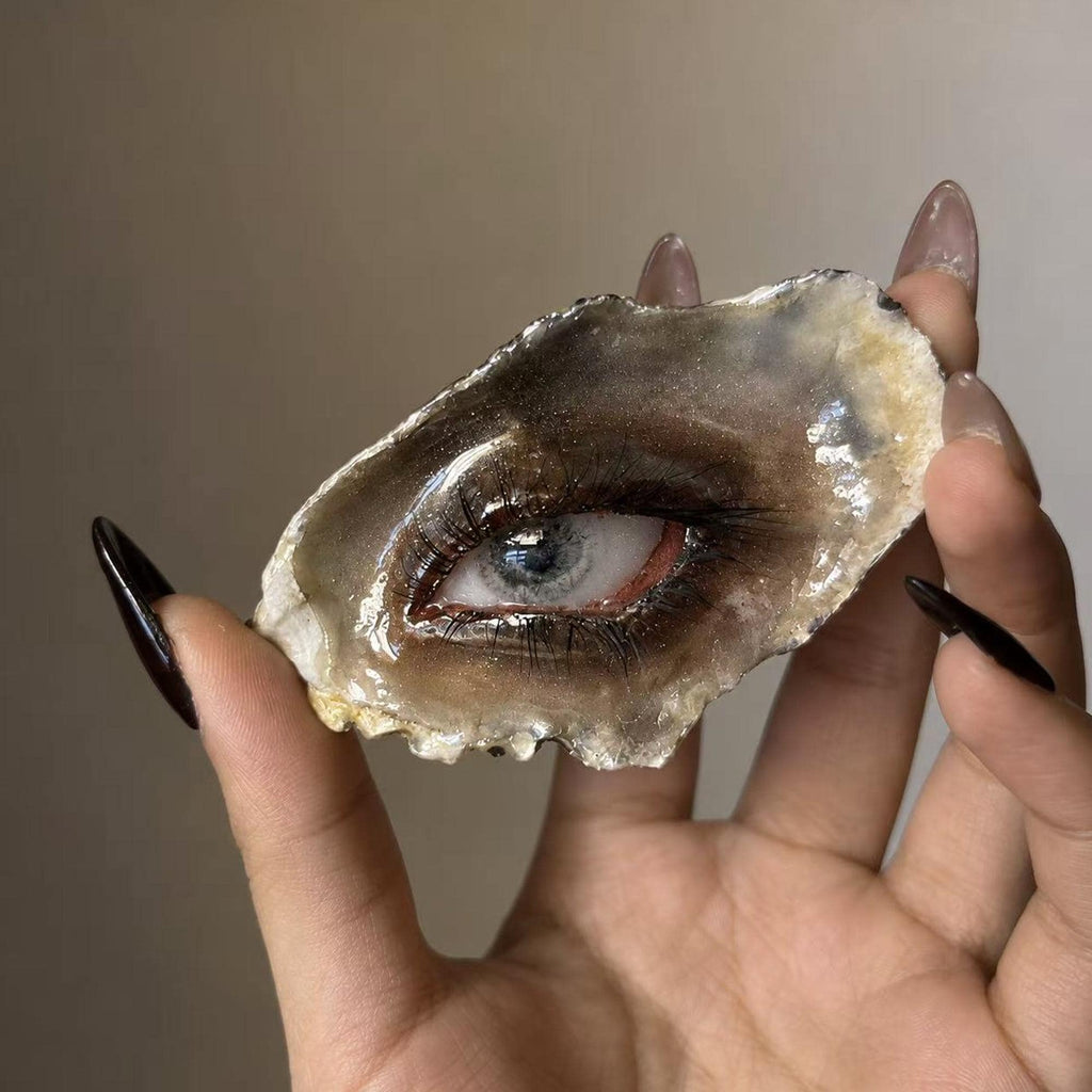 Lilith Grey Temptation oyster eye held between fingers, showing its irregular shell edge.