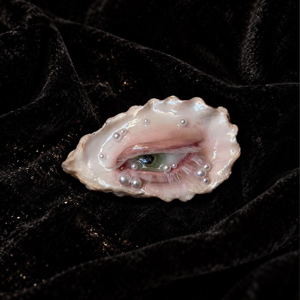 Nyra Nacre Veil oyster eye with scattered pale beads on black velvet.