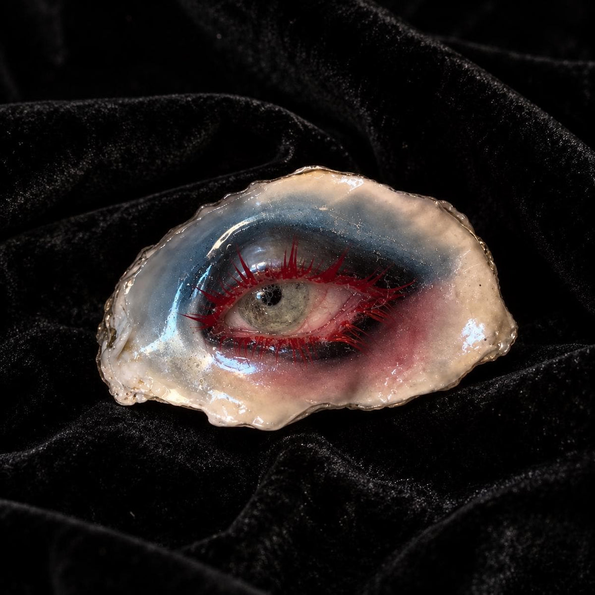 Lilith Thorned Gaze oyster eye with red lashes and a pale iris on black velvet.