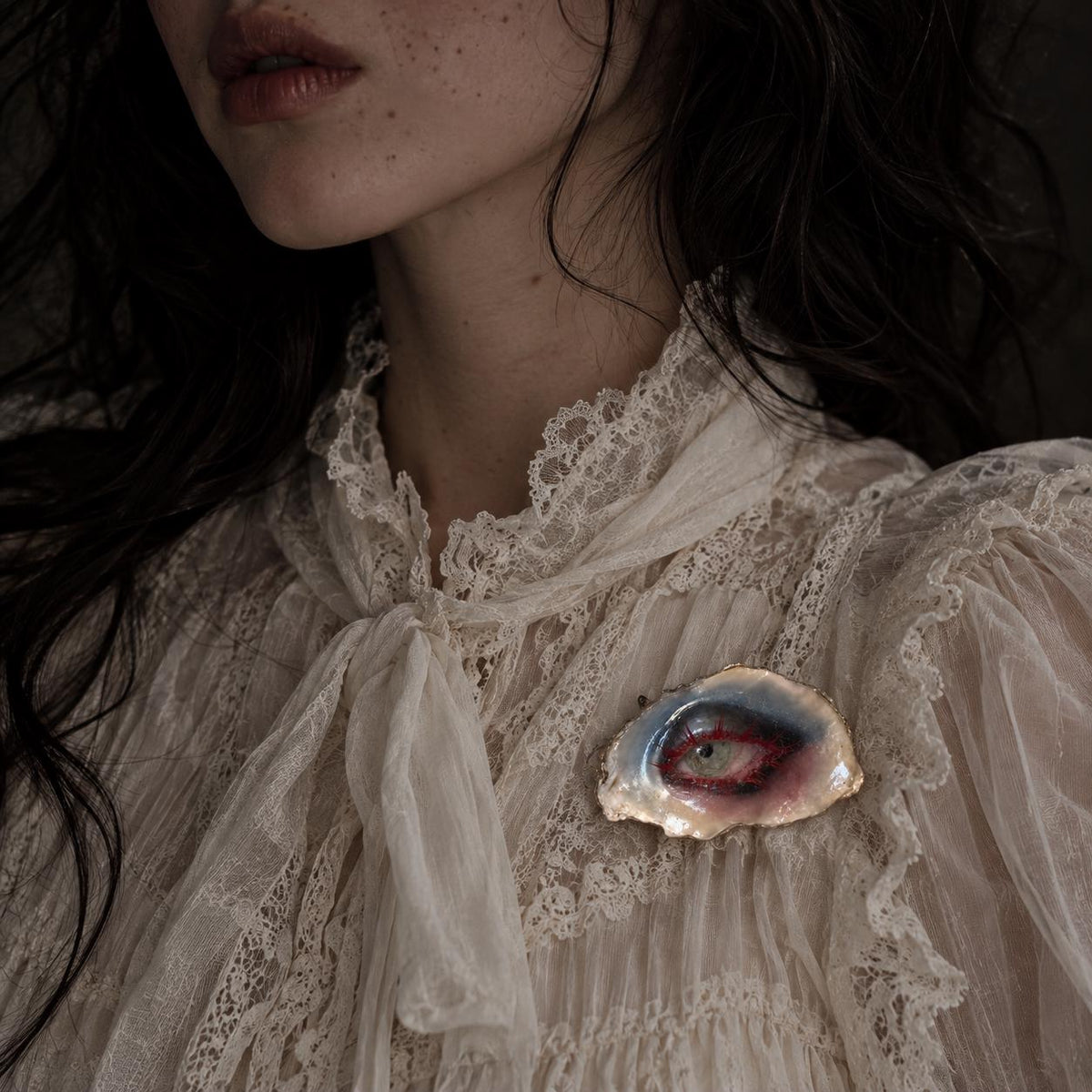 Lilith Thorned Gaze shell-eye brooch worn on an ivory lace blouse.