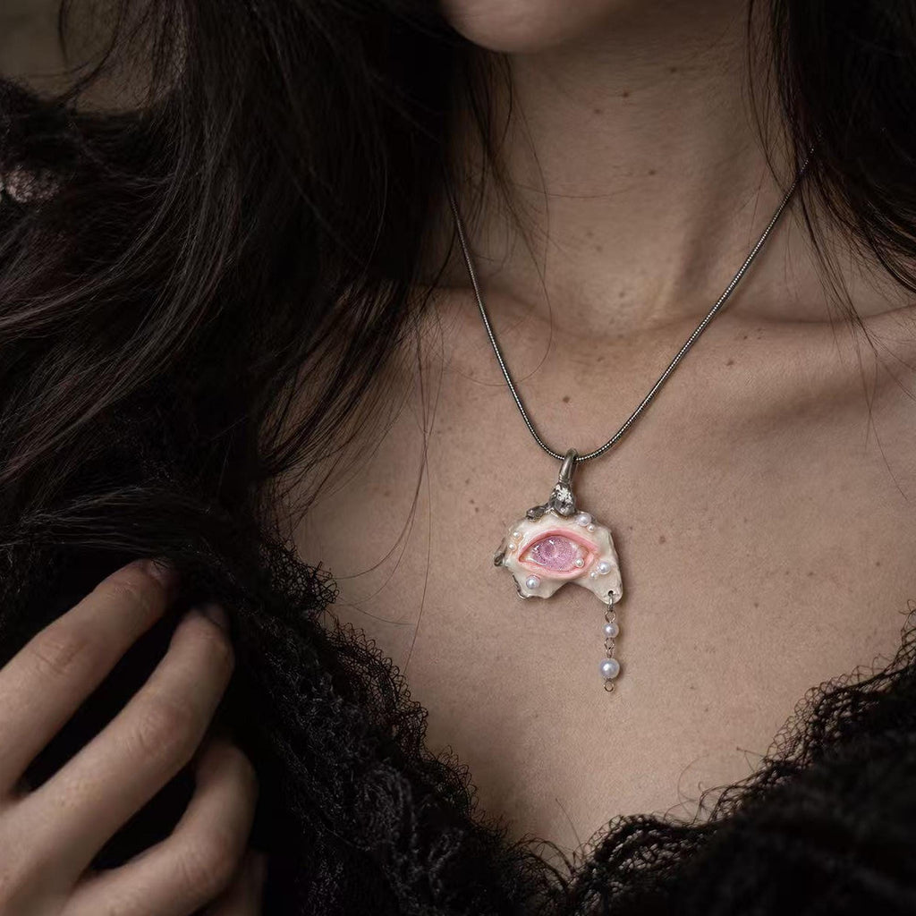 Pink-eyed Nyra shell pendant with a hanging bead drop worn on a metal chain.