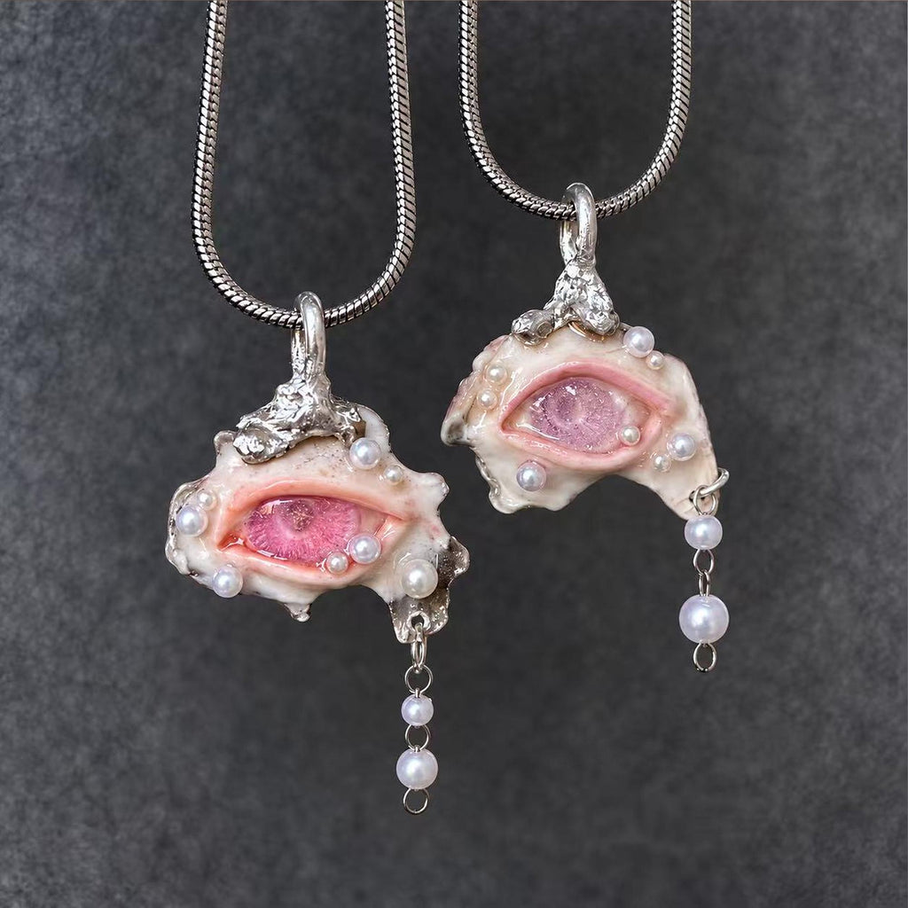 Two pink-eyed Nyra shell pendants with bead drops displayed on black velvet.