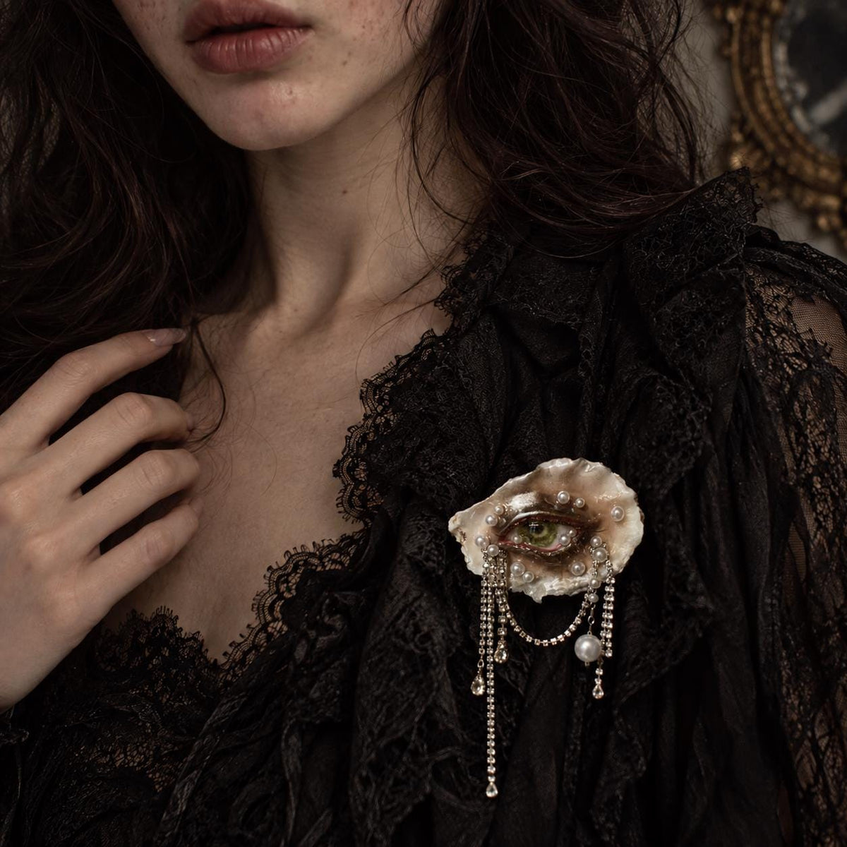 Lilith Veil Emerald Siren shell-eye brooch worn on black lace.